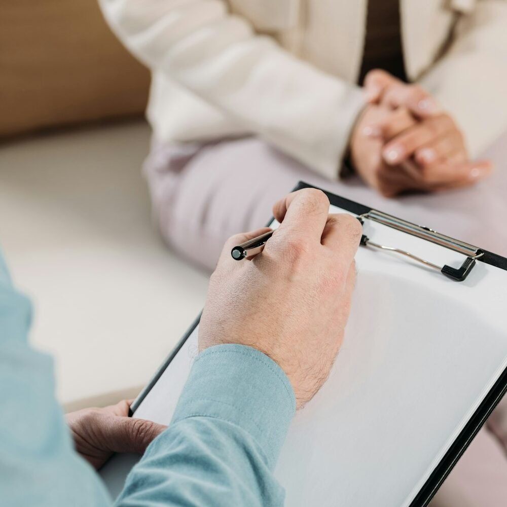 cropped shot of psychotherapist writing on clipboard and female patient sitting on couch