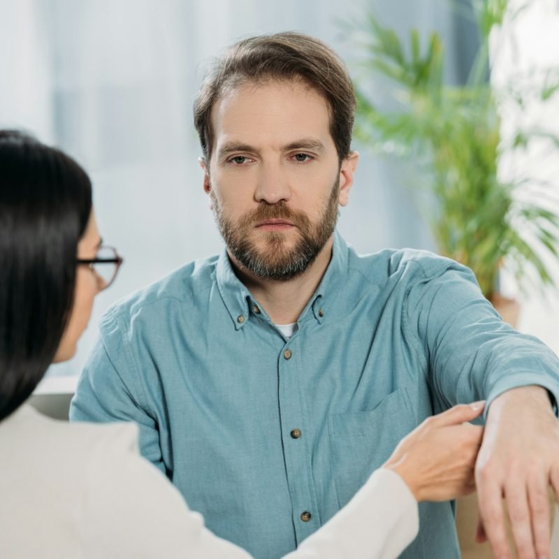 young woman in eyeglasses holding hand of bearded man during hypnotherapy